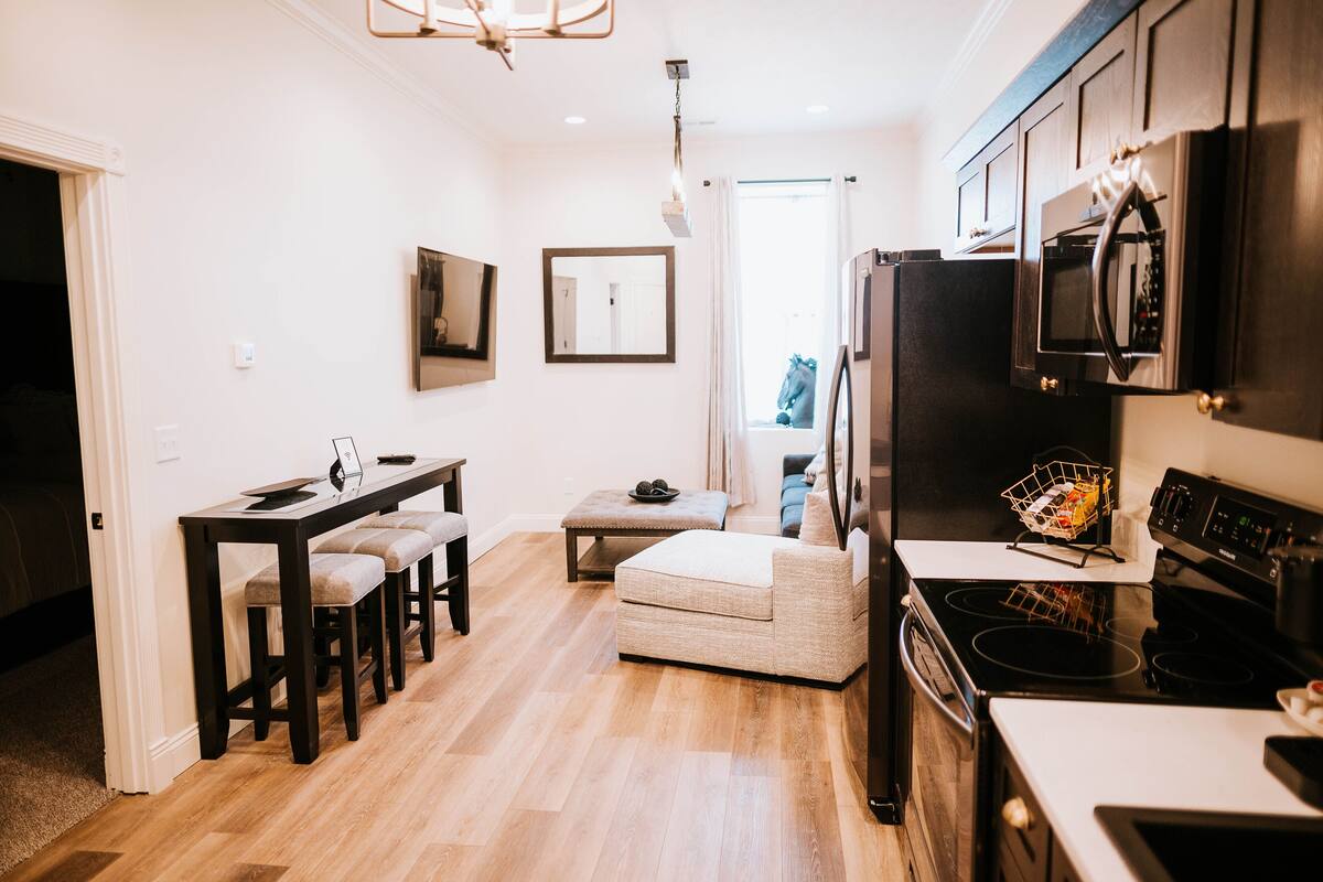 A modern kitchen with a dining area, wooden flooring, and a view to the outside.