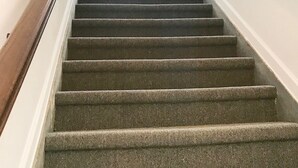 A staircase with carpeted steps, white walls, and a chandelier. - Inn On Central (Le Mars)