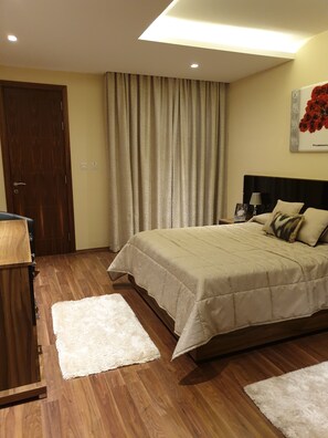 Ein Schlafzimmer mit Bett, Schreibtisch, Stuhl, weißem Teppich, Holzboden, Tür und Vorhang.