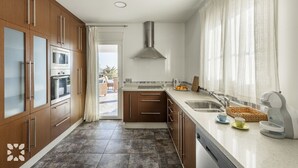 Ett modernt kök med träskåp, en rostfri köksfläkt och ett stort fönster med tunna, genomskinliga gardiner.