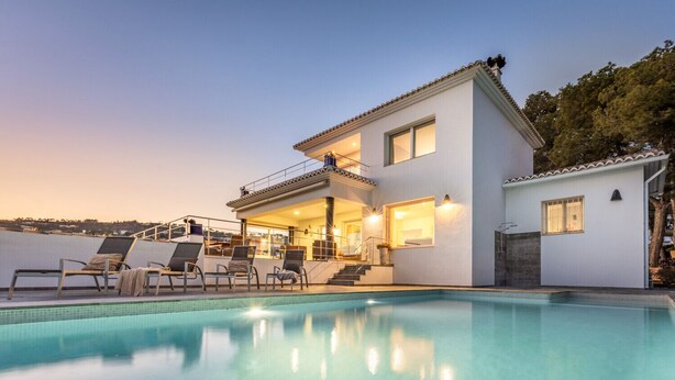 Ett modernt hus i två våningar med en swimmingpool, en uteplats och en balkong med utsikt över havet.