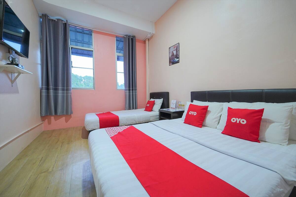 A hotel room with two beds, a TV, a window with curtains, and a poster on the wall.