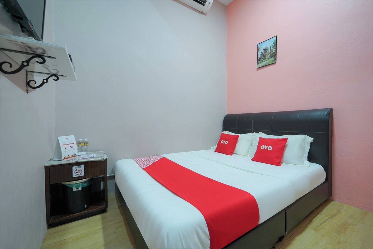 A hotel room with a bed, a nightstand, a trash bin, and a wall-mounted air conditioner.