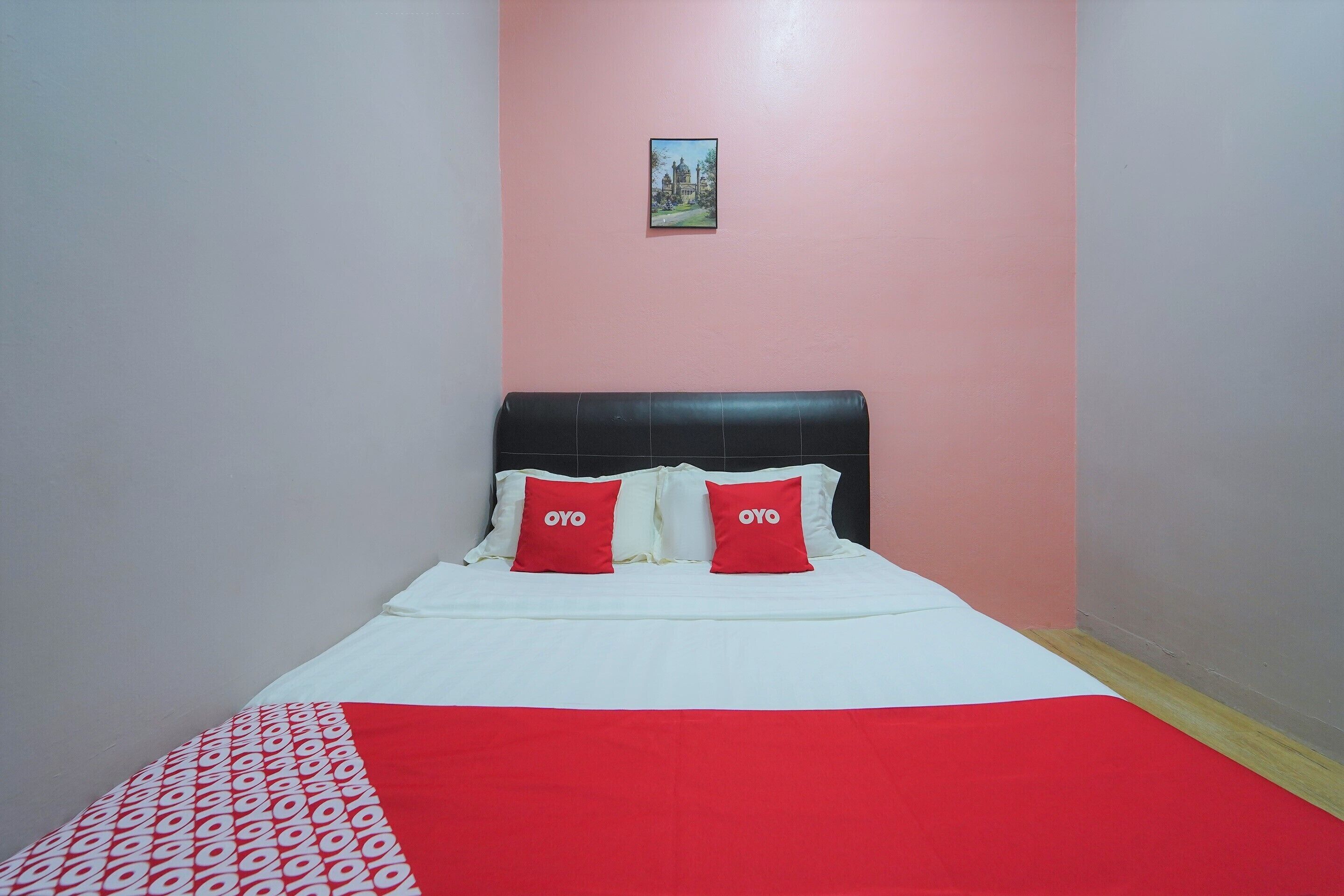 A bed with a white and red bedspread, two red pillows with the word "OYO" on them, and a small framed picture on the wall above the bed.