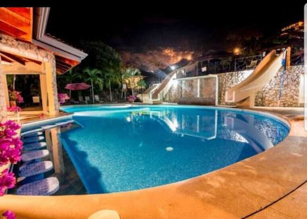 Surrounded by a stone wall, the pool features a small waterfall and a covered seating area.