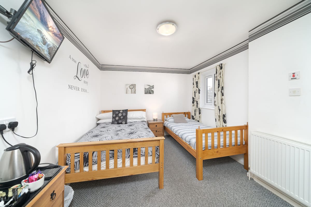 A bedroom with two wooden beds, a TV mounted on the wall, a kettle on a table, and a radiator.