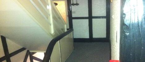 A narrow staircase with a carpeted floor leading to a room with a dark wooden door.