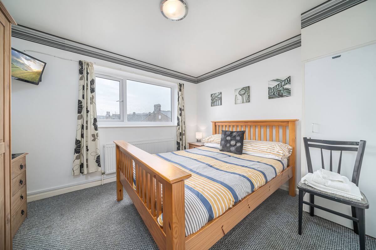 A bedroom with a wooden bed, a chair, a window with curtains, and a radiator.
