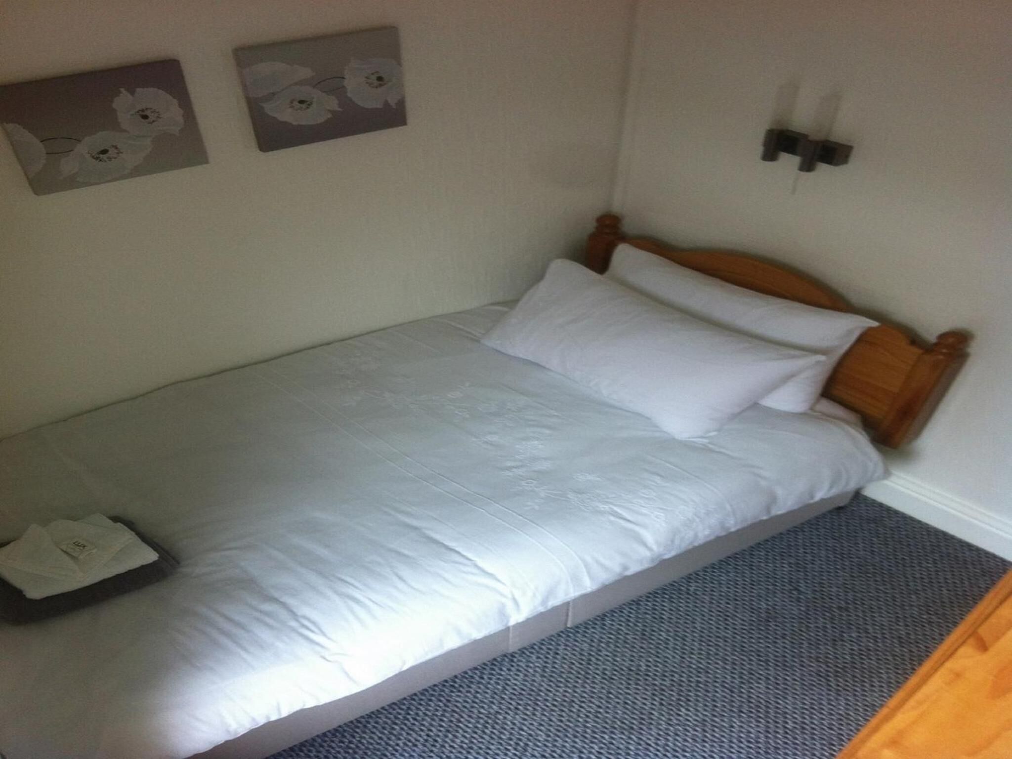 A single bed with white bedding, a wooden headboard, and a gray carpeted floor.