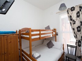 Een slaapkamer met een stapelbed, een houten hoofdbord, een bureau, een stoel en een raam met bloemen gordijnen.