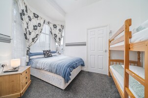 Een slaapkamer met een bed, nachtkastje, dressoir, een stapelbed en een deur.