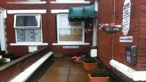 A narrow alleyway with a reception sign, a green awning, and potted plants. - Deneside Guest House (Blackpool)