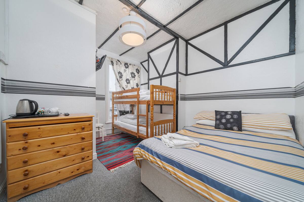 A room with a bunk bed, a wooden dresser, a striped bedspread, and a patterned pillow.