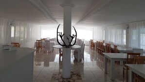 A spacious dining area with white tables and chairs, a central decorative column, and large windows allowing natural light. - Hotel Tsalka (Tsalka)