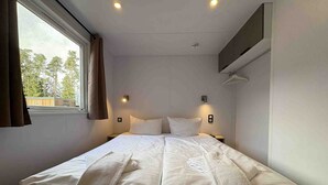 Una cama individual con ropa de cama y toallas blancas, una ventana con cortinas y un aire acondicionado instalado en la pared.