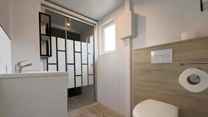 Un baño con inodoro, zona de ducha y soporte para papel higiénico en la pared.