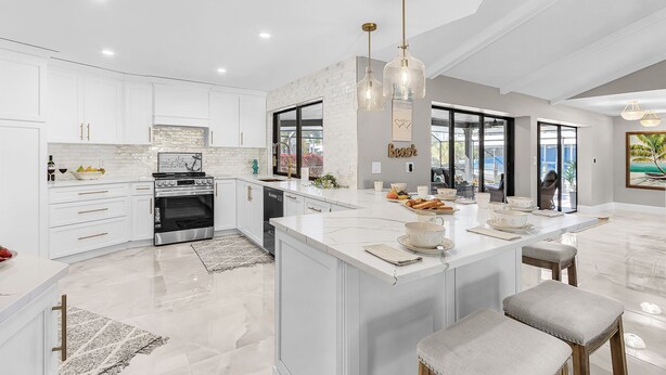 Una cocina moderna con armarios blancos, una isla grande, electrodomésticos de acero inoxidable e iluminación colgante.