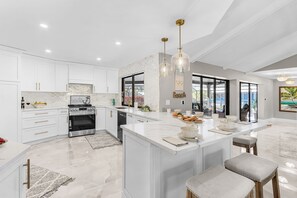 Une cuisine moderne avec des meubles blancs, un grand îlot central, des appareils en acier inoxydable et des luminaires suspendus.