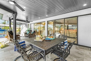 Un área de comedor al aire libre con techo, una mesa y sillas, una piscina al fondo y vistas del paisaje circundante.