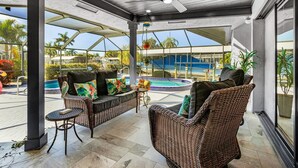 Un espacio de estar al aire libre cubierto con mobiliario de mimbre y vistas a una piscina.