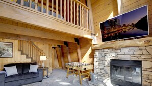 A cozy room with a stone fireplace, a foosball table, a sofa, and a cityscape painting. - Switzerland SKI Chalet #845 (Big Bear Lake)