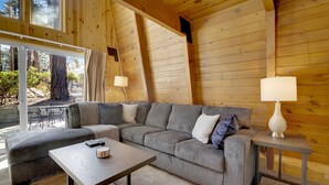A modern log cabin interior with a gray sectional sofa, a small table, and a lamp. - Switzerland SKI Chalet #845 (Big Bear Lake)