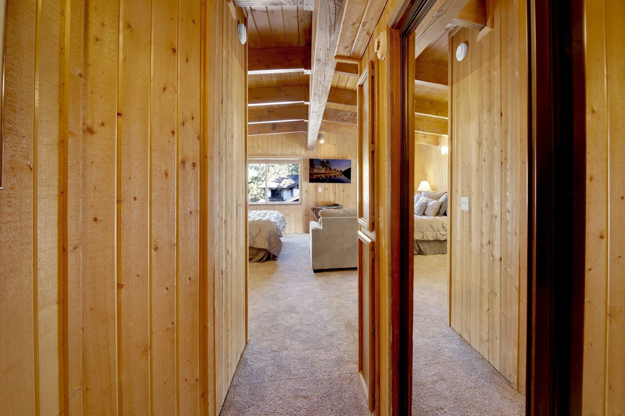 A wooden interior hallway leading to a bedroom with a bed and a sofa.