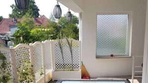 Un patio techado con una mesa de vidrio, muebles de mimbre, un ventanal con vidrio esmerilado y vistas a casas vecinas.