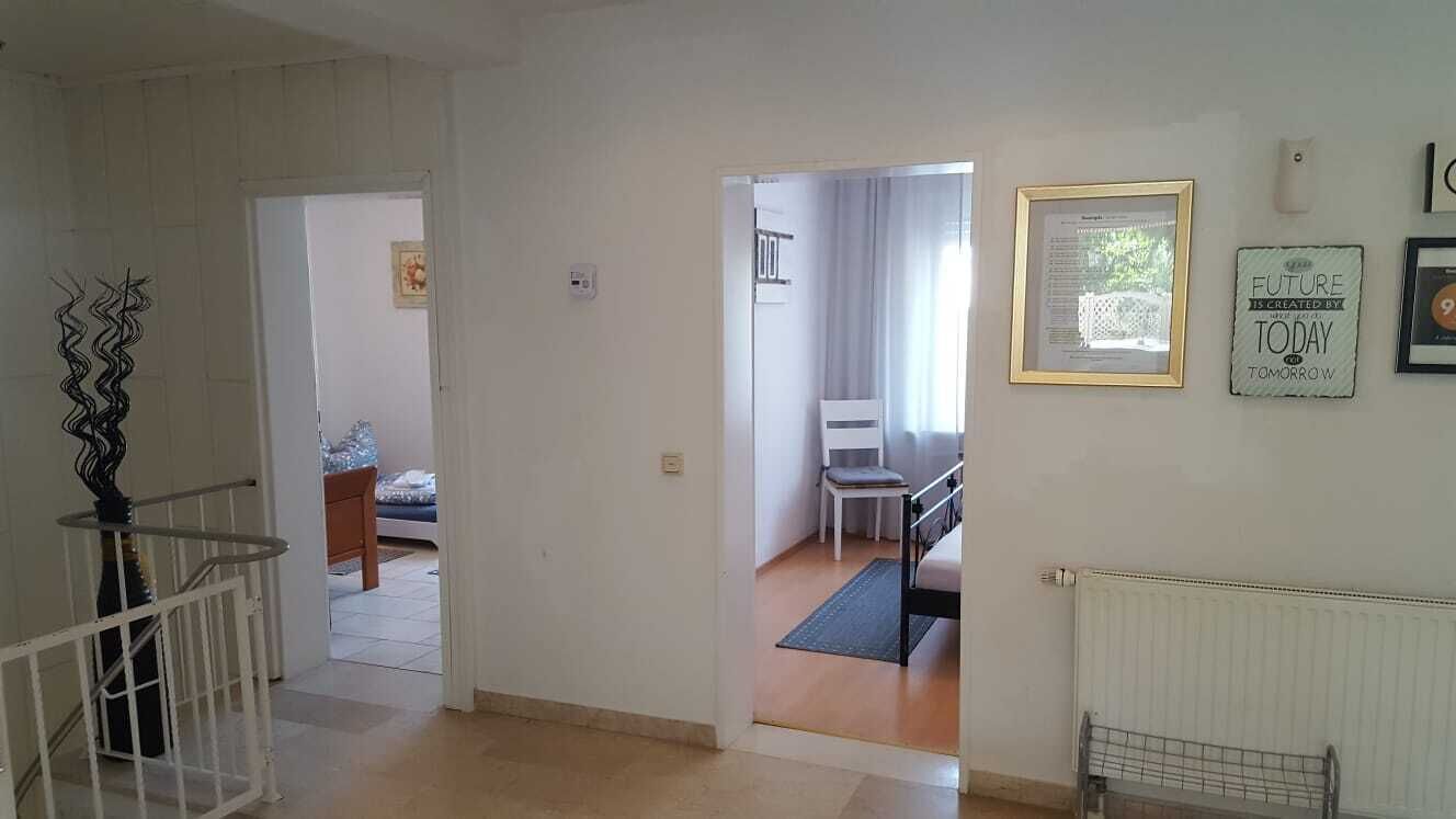 Ein Flur mit Treppe, einer Tür zu einem Zimmer mit Bett und einer Heizung.