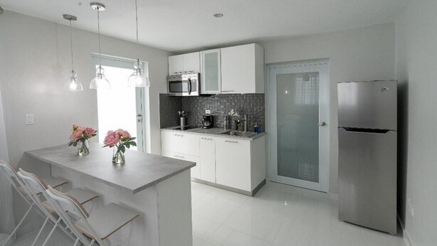 A modern kitchen with white cabinets, a stainless steel refrigerator, and a bar area with stools. - Beautiful modern apartment close to airport and the beach (Cangrejo Arriba, Carolina, Puerto Rico)
