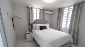 A bedroom with a bed, a nightstand, a hanging coat rack, and a window with curtains. - Beautiful modern apartment close to airport and the beach (Cangrejo Arriba, Carolina, Puerto Rico)