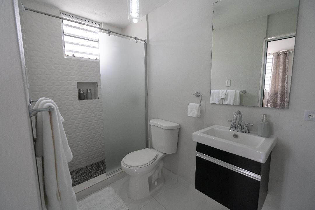 Et badeværelse med bruser, toilet, vask og et stort spejl.