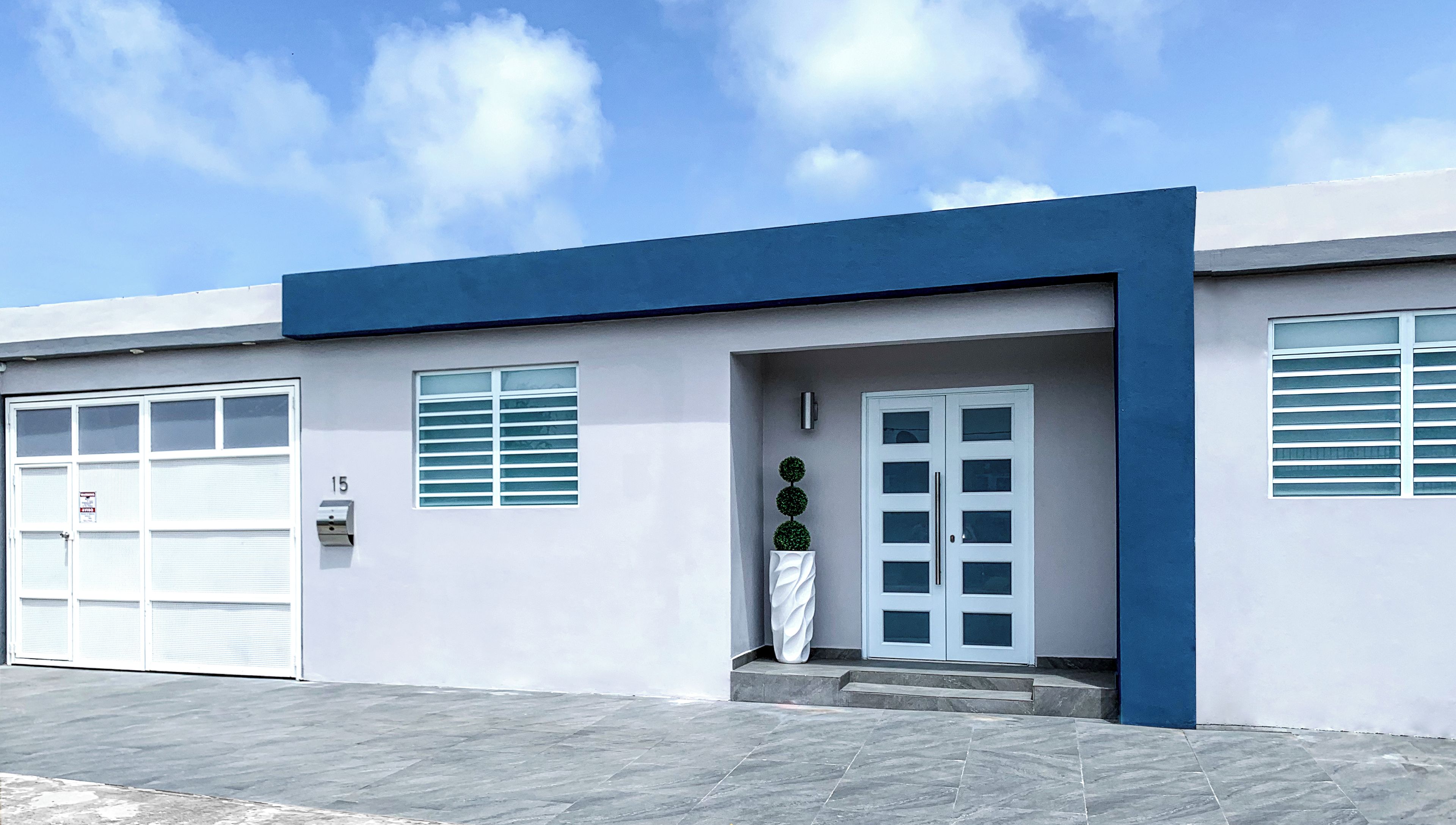A modern building with a blue and white facade, a garage door, and a large potted plant in front.