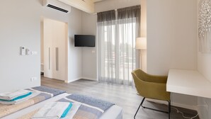 Ett modernt hotellrum med en säng, ett skrivbord, en stol, en TV och ett fönster med gardiner.
