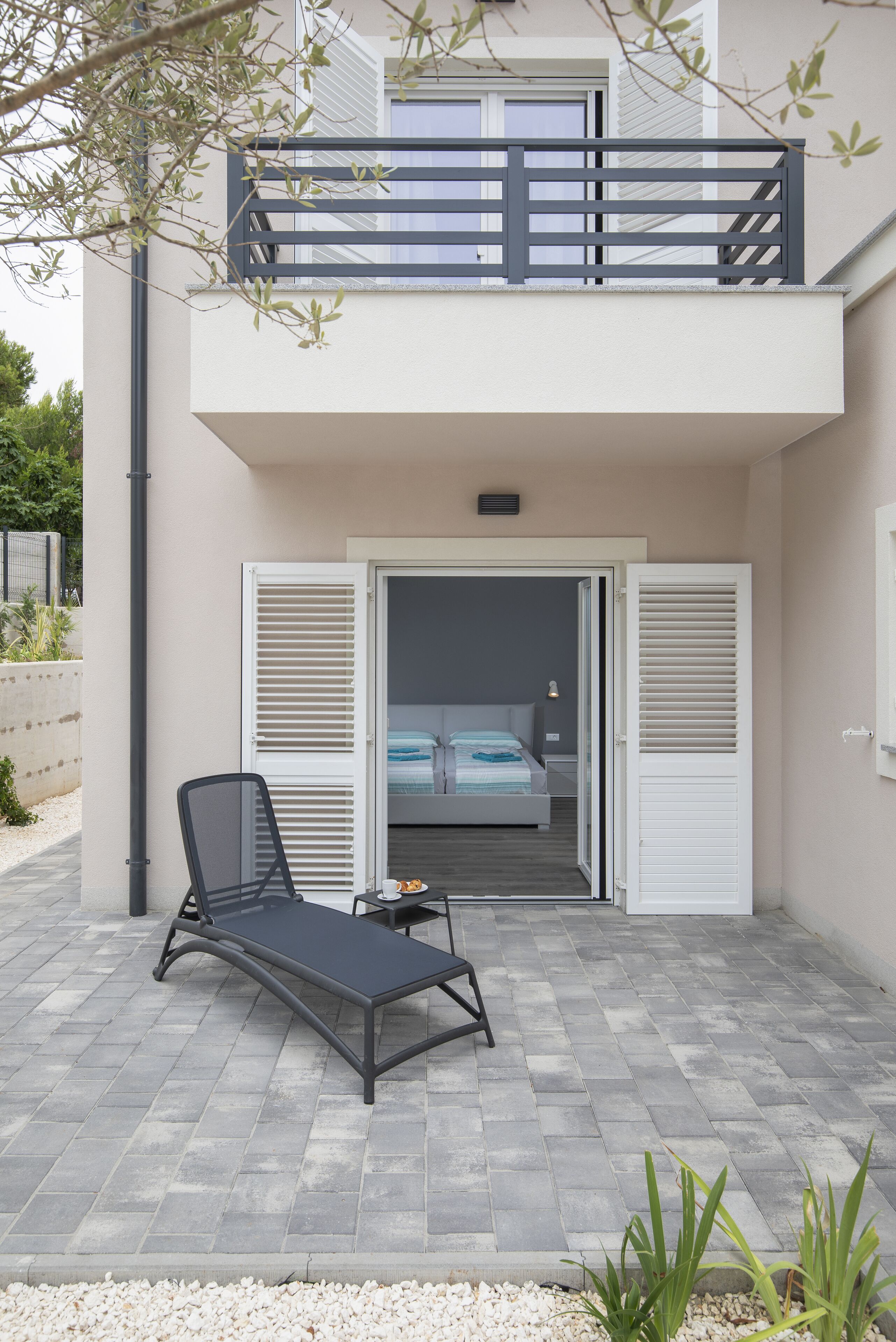 A two-story building with a balcony, a lounge chair, and a bed visible through open shutters.