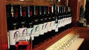 Una dispensa per vino con diverse bottiglie e un bicchiere di vino rosso.