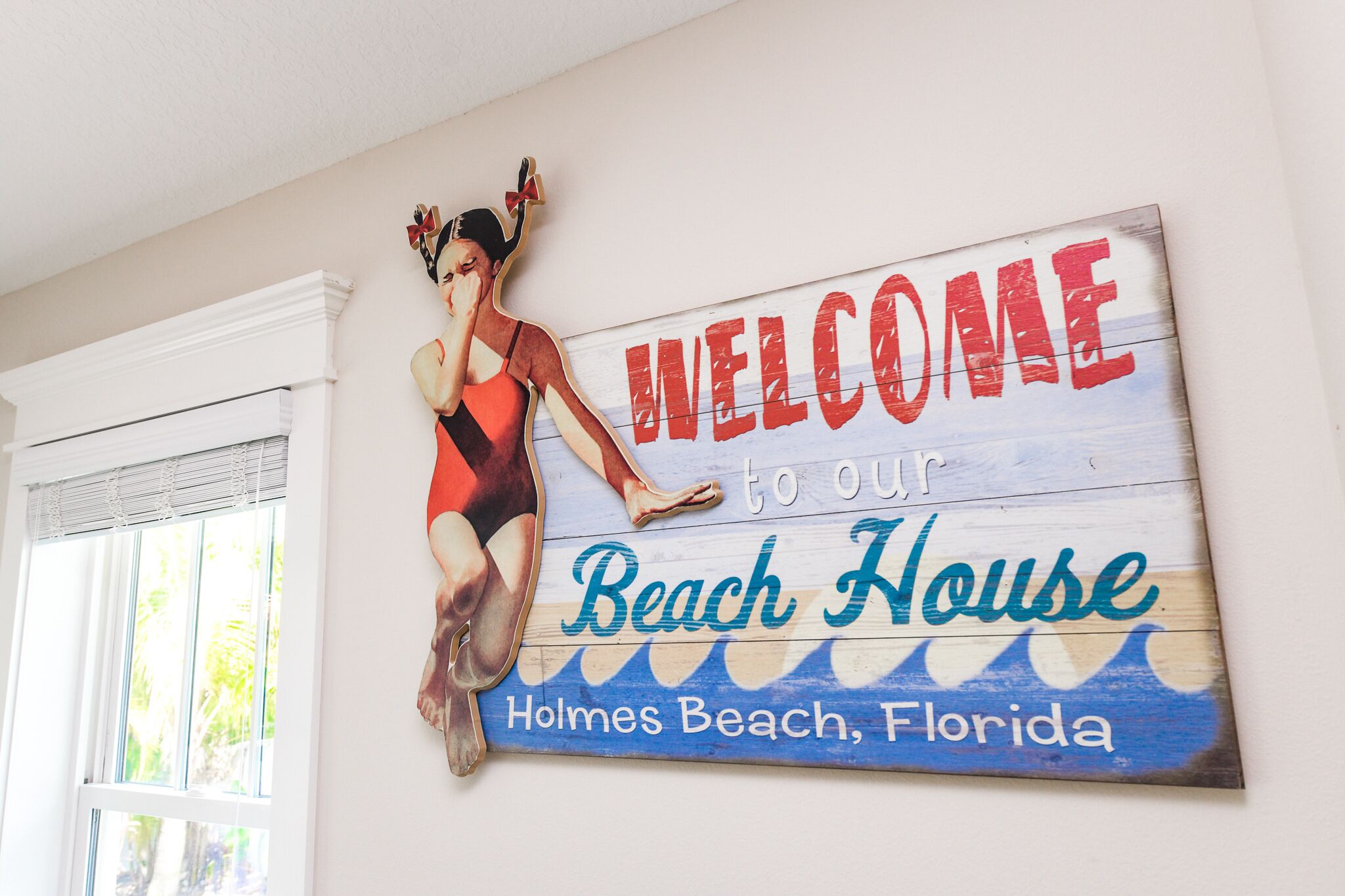 A welcome sign for a beach house in Holmes Beach, Florida, featuring a woman in a swimsuit.