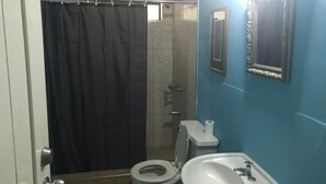 A bathroom with a shower curtain, toilet, sink, and a mirror on the wall. - Manor Park Private Room (Constant Spring)