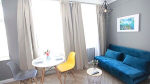 Ein modernes Wohnzimmer mit einem blauen Sofa, einem gelben Sessel, einem weißen Tisch und einem Gemälde an der Wand.