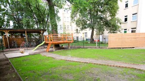 Ein Spielplatz mit einer Rutsche und einer Holzkonstruktion, umgeben von Gras und Bäumen.
