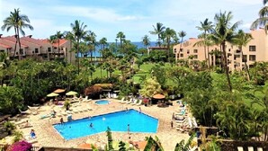 A resort with a central swimming pool, lounge areas, and palm trees.
