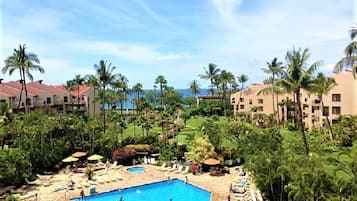 A resort with a central swimming pool, lounge areas, and palm trees.