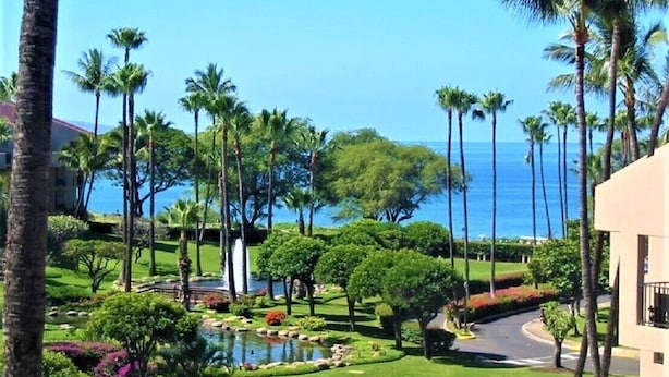 A resort with a well-maintained garden, palm trees, and a view of the ocean.