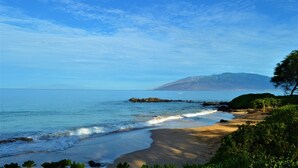 A beach with clear skies, calm waters, and distant mountains.