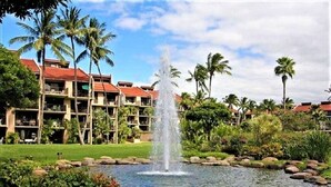A hotel with a water fountain, palm trees, and a well-maintained lawn.