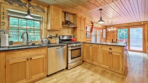Cocina de cabaña de madera con una isla grande, electrodomésticos de acero inoxidable y vistas al exterior.