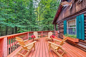 Un pontile di legno con poltrone Adirondack, un rifugio in legno con persiane verdi e uno sfondo boschivo.