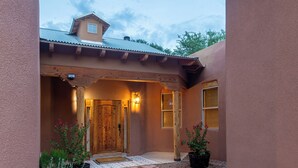A house with a stone pathway leading to a wooden door, surrounded by a garden with various plants.
