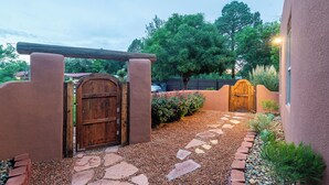 A pathway leading to a wooden gate, surrounded by a gravel area and a small garden with cacti and shrubs.