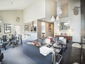 A modern living room with a large sectional sofa, a dining area with a glass table and chairs, and a kitchen area with a built-in stove. - Vantage Point Condo 601 (Vail)